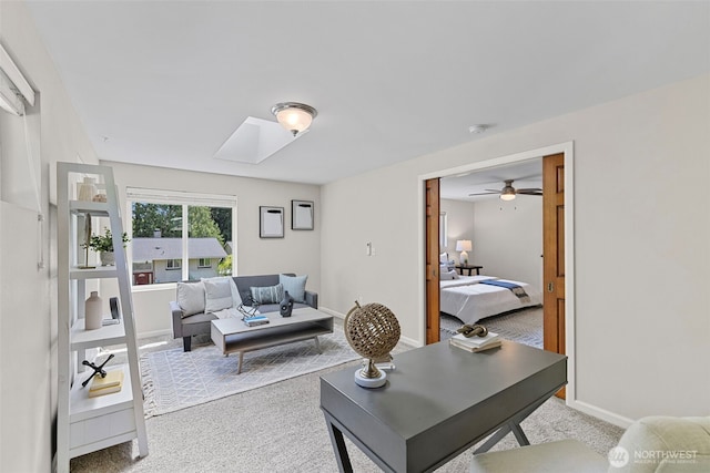 living area with baseboards, ceiling fan, a skylight, and light carpet
