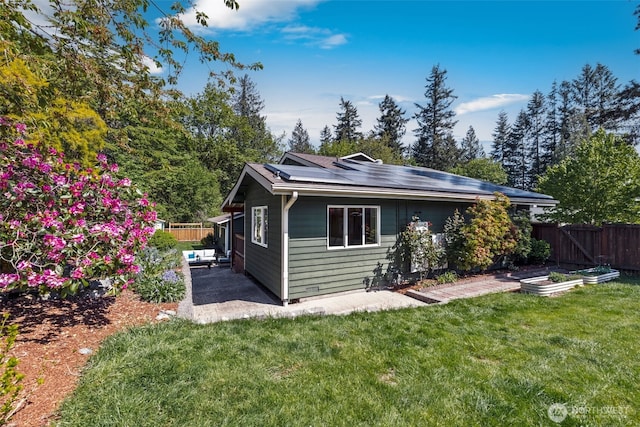back of house with a fenced backyard, roof mounted solar panels, a patio area, and a yard