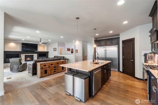 kitchen featuring stainless steel appliances, a sink, light wood-type flooring, ceiling fan, and light countertops