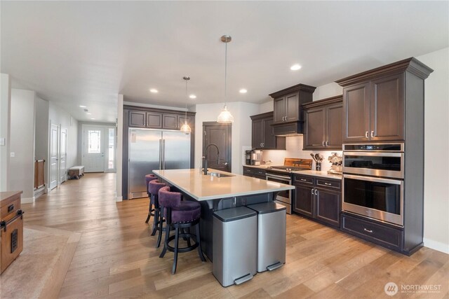 kitchen featuring a sink, appliances with stainless steel finishes, light wood-type flooring, a breakfast bar, and light countertops