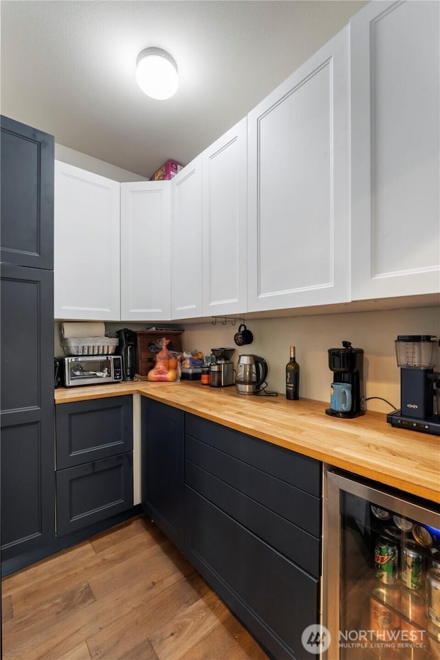 kitchen featuring butcher block countertops, wine cooler, light wood-style flooring, and white cabinets