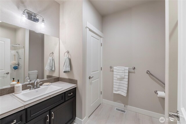 full bath featuring toilet, baseboards, vanity, and a shower