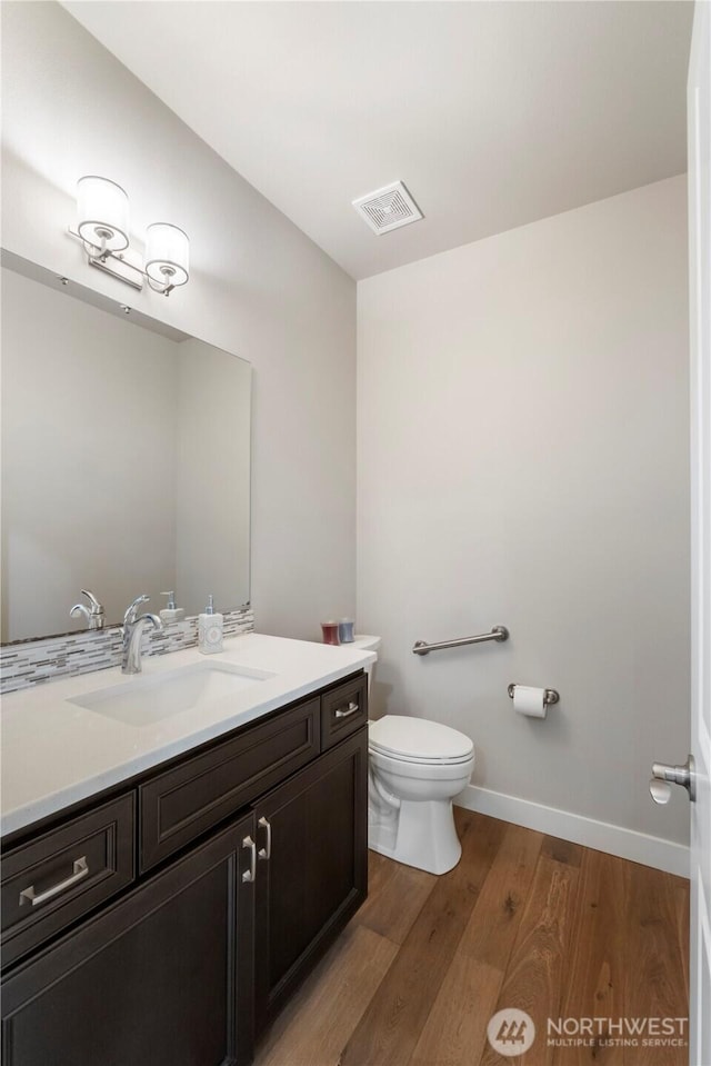 half bathroom with wood finished floors, toilet, vanity, and baseboards