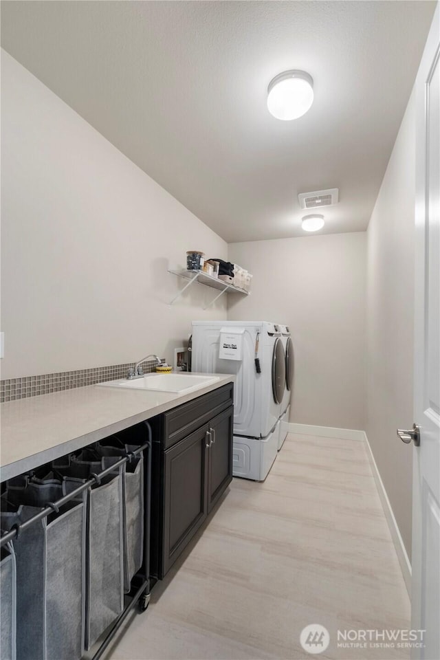 clothes washing area featuring washing machine and clothes dryer, light wood-type flooring, cabinet space, and baseboards