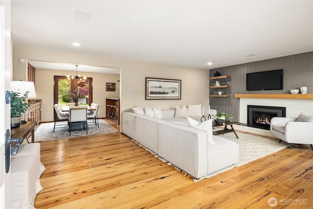 living area featuring a brick fireplace, recessed lighting, a notable chandelier, and light wood-style flooring