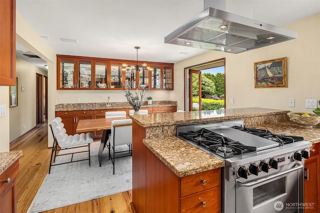 kitchen featuring brown cabinets, extractor fan, stainless steel stove, and light wood-style floors