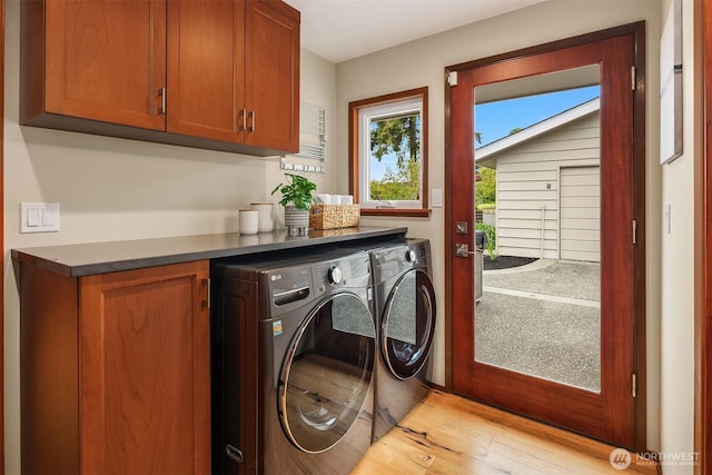 clothes washing area with light wood finished floors, cabinet space, and washer and clothes dryer