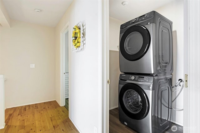 clothes washing area with laundry area, stacked washer and dryer, light wood-style floors, and baseboards