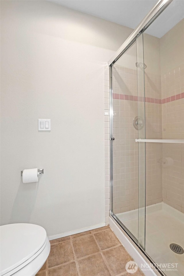 bathroom with baseboards, a shower stall, and toilet
