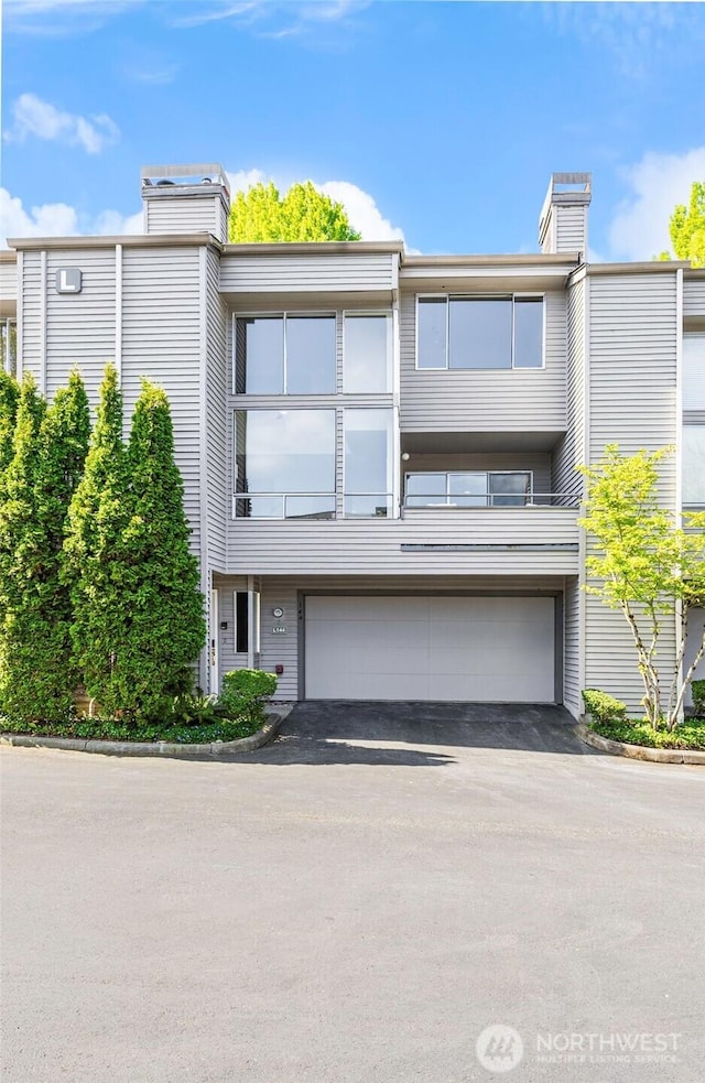 multi unit property featuring an attached garage, a chimney, and driveway