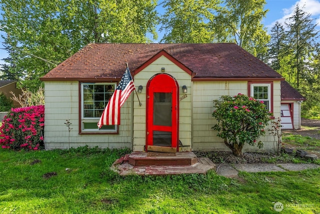 bungalow featuring a garage, a shingled roof, and a front lawn