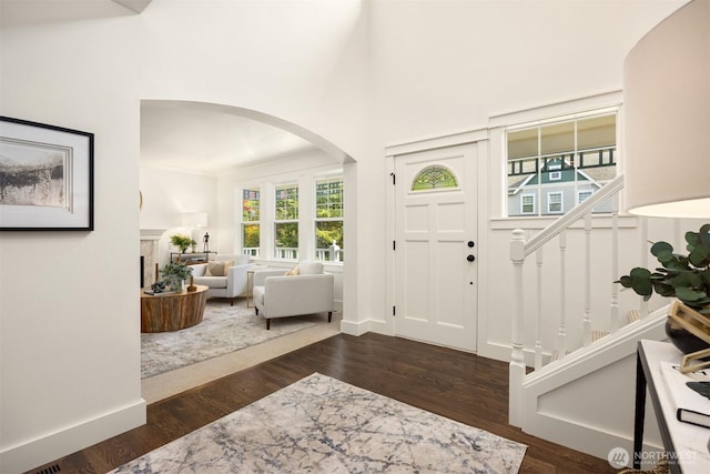 entrance foyer featuring arched walkways, dark wood-style flooring, a towering ceiling, and stairway