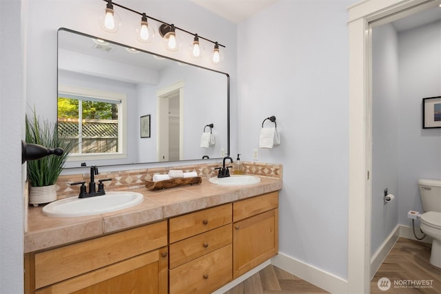 bathroom with a sink, baseboards, toilet, and double vanity