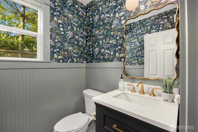 bathroom featuring vanity, toilet, wallpapered walls, and a wainscoted wall