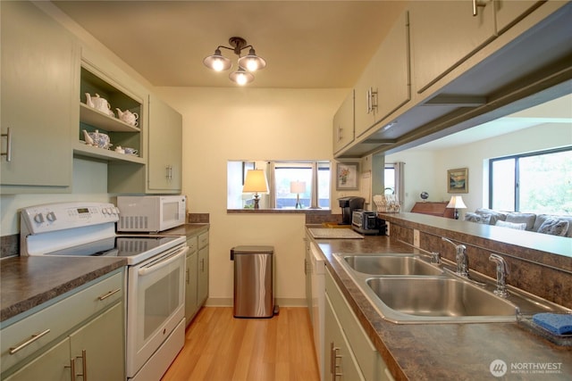 kitchen with a sink, light wood-style flooring, dark countertops, and white appliances