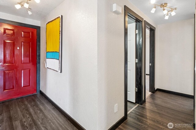 corridor with an inviting chandelier, baseboards, rail lighting, and dark wood-style floors