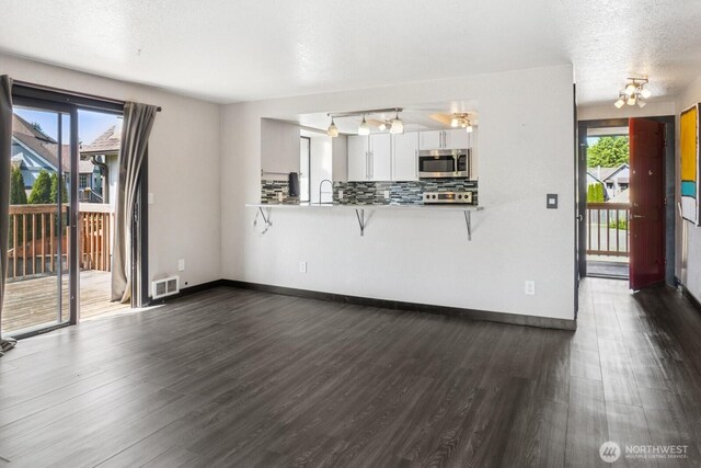 unfurnished living room featuring a sink, dark wood-style flooring, and a wealth of natural light