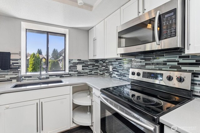 kitchen with backsplash, appliances with stainless steel finishes, a sink, light countertops, and white cabinets