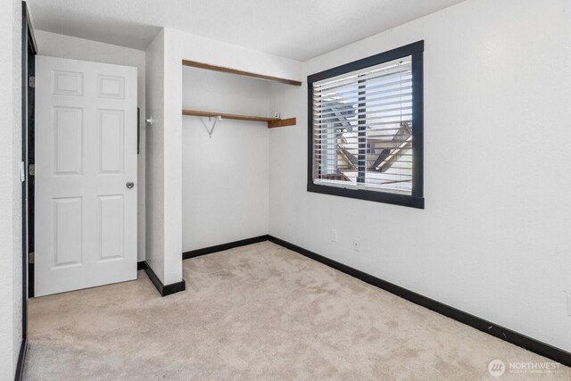 unfurnished bedroom featuring baseboards, light carpet, and a closet