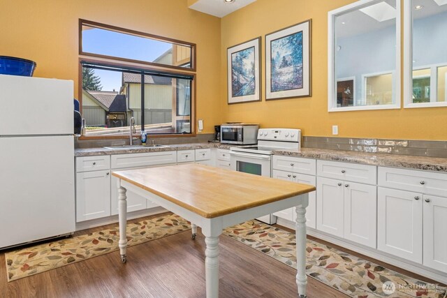 kitchen featuring wood finished floors, white appliances, light stone countertops, white cabinets, and a sink