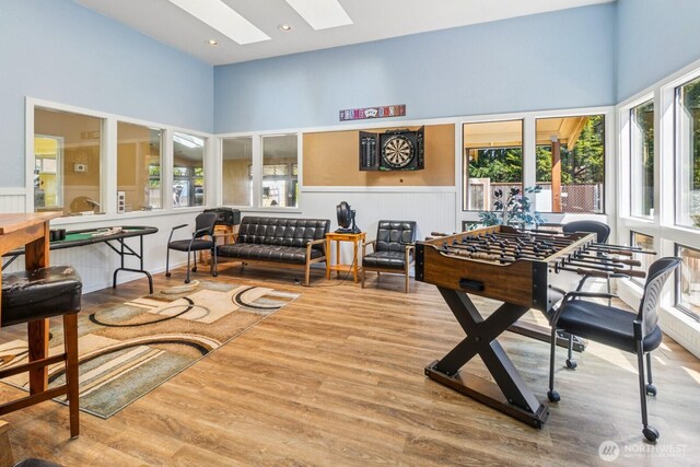 rec room with wood finished floors, a wainscoted wall, and a skylight