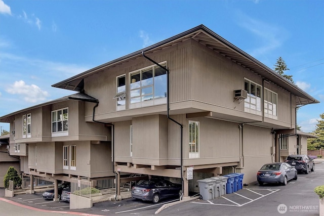 view of front of house featuring covered and uncovered parking and a wall unit AC