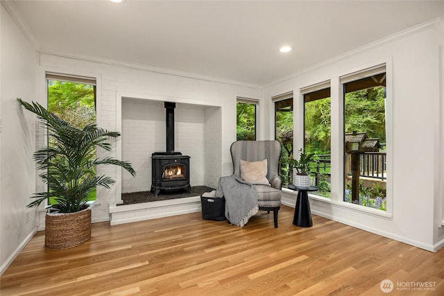 sitting room featuring crown molding, a wood stove, baseboards, and light wood-type flooring