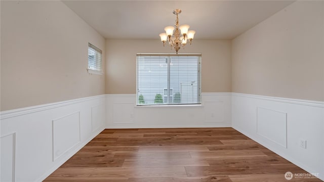 spare room featuring wood finished floors, a wainscoted wall, and a chandelier