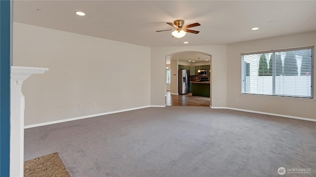 empty room with carpet floors, a ceiling fan, baseboards, recessed lighting, and arched walkways