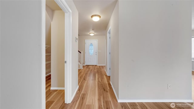 hall featuring light wood-type flooring, baseboards, and stairs