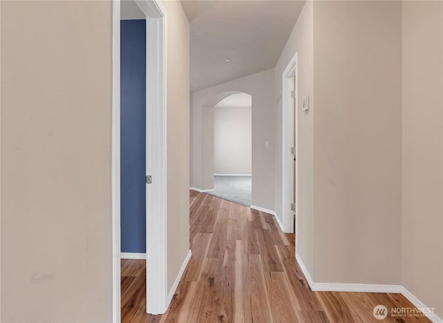 corridor with baseboards, arched walkways, and light wood-style flooring