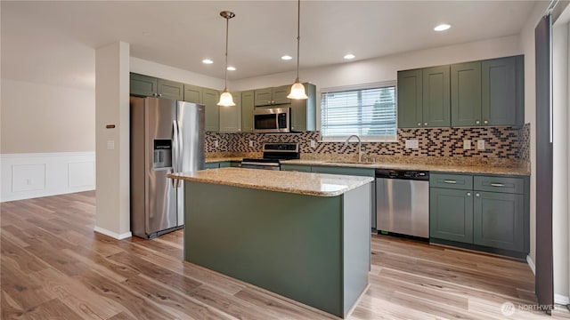 kitchen with appliances with stainless steel finishes, light stone countertops, a sink, green cabinets, and light wood-style flooring