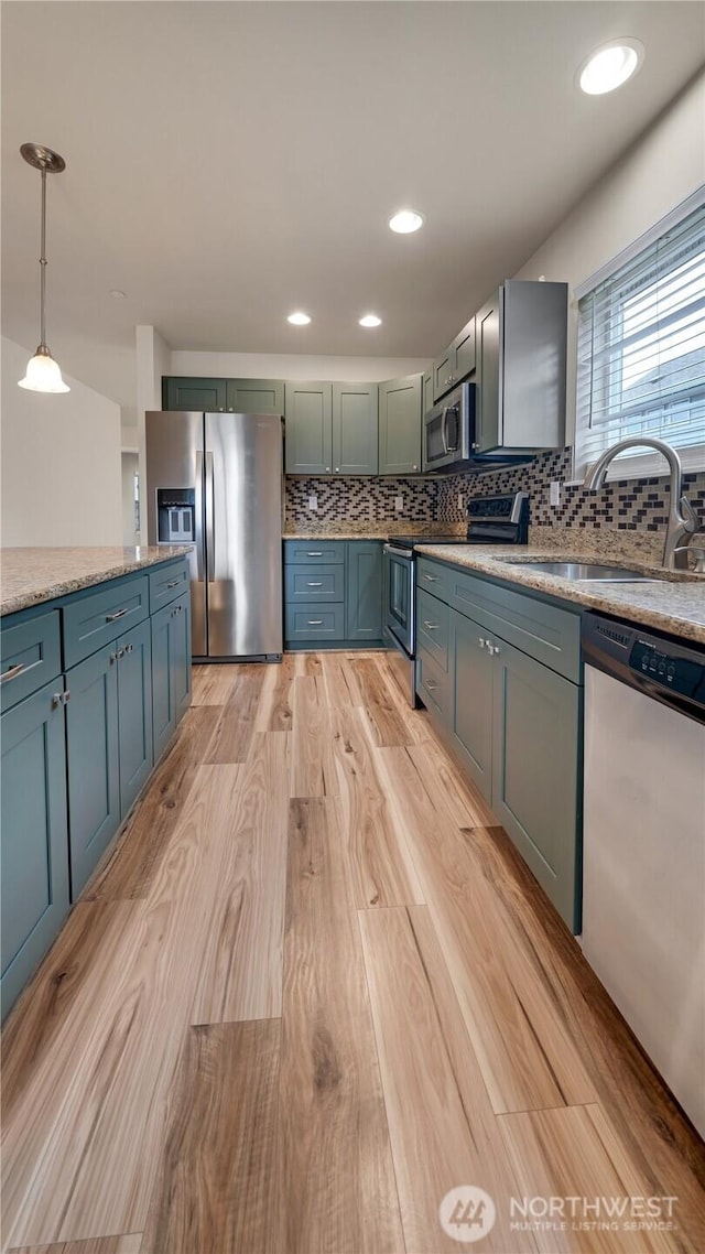 kitchen with decorative backsplash, pendant lighting, light wood-type flooring, a sink, and appliances with stainless steel finishes