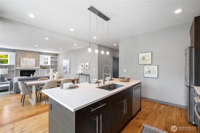 kitchen with appliances with stainless steel finishes, a sink, light wood-style floors, light countertops, and a center island with sink