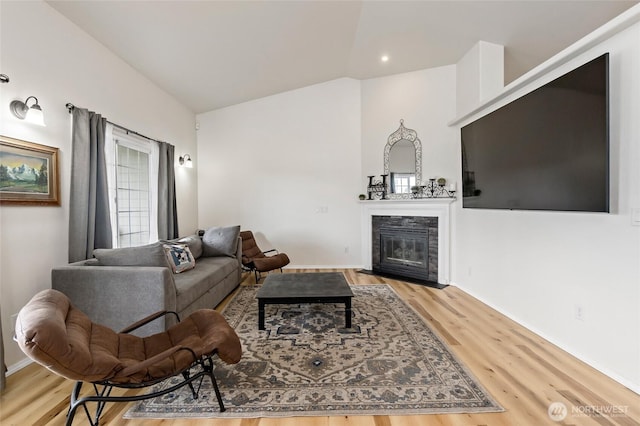 living room featuring baseboards, a fireplace with flush hearth, wood finished floors, and vaulted ceiling