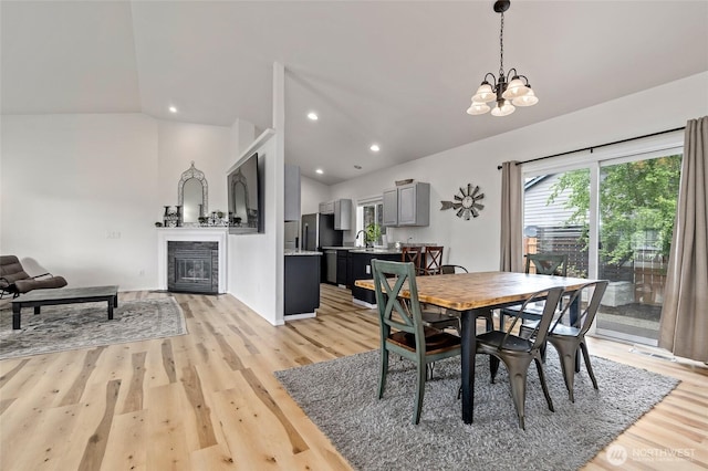 dining space featuring light wood-style floors, a glass covered fireplace, lofted ceiling, and a chandelier