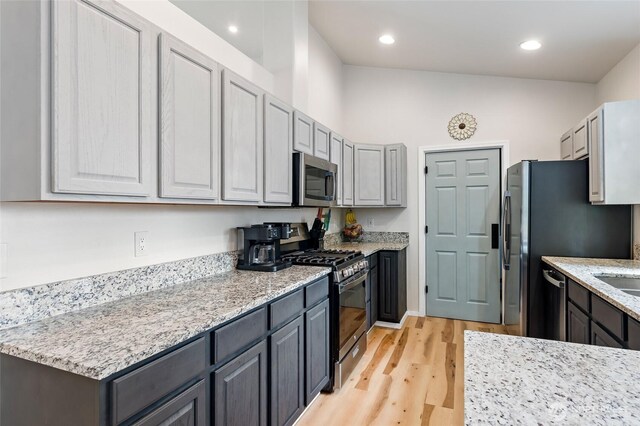 kitchen featuring appliances with stainless steel finishes, light stone counters, light wood finished floors, gray cabinets, and recessed lighting