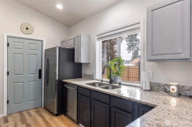 kitchen with a sink, light wood finished floors, dishwasher, and light stone countertops