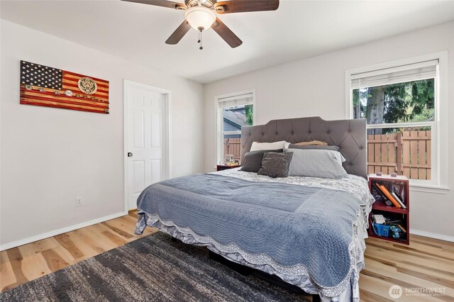 bedroom featuring baseboards, ceiling fan, multiple windows, and wood finished floors