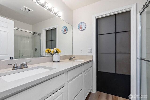 full bathroom featuring visible vents, a sink, an enclosed shower, and double vanity