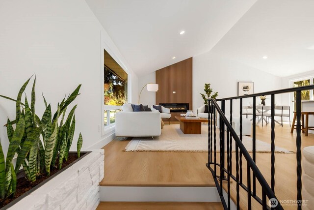 hall with an upstairs landing, wood finished floors, and lofted ceiling