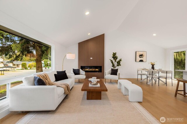 living area featuring recessed lighting, light wood finished floors, vaulted ceiling, and a large fireplace