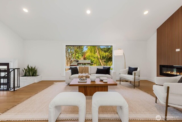 living area with recessed lighting, baseboards, a glass covered fireplace, and wood finished floors