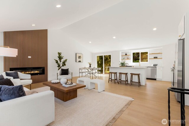 living area featuring recessed lighting, a glass covered fireplace, lofted ceiling, and light wood-style floors