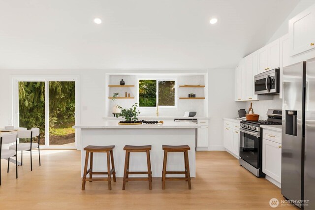 kitchen featuring open shelves, appliances with stainless steel finishes, a breakfast bar, and light countertops