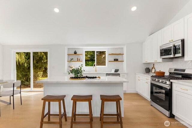 kitchen featuring open shelves, a kitchen breakfast bar, a center island, white cabinets, and stainless steel appliances