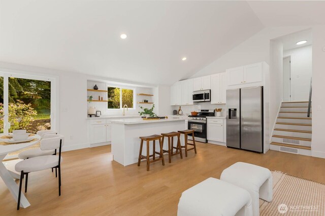 kitchen with open shelves, lofted ceiling, a kitchen island, a breakfast bar, and appliances with stainless steel finishes
