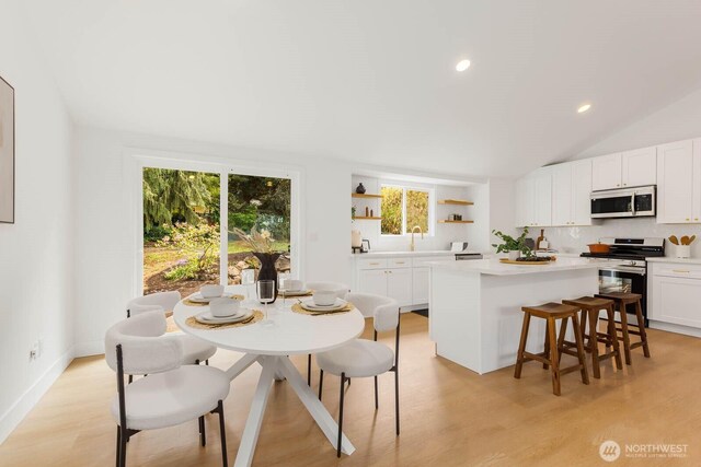 kitchen with open shelves, appliances with stainless steel finishes, light countertops, a breakfast bar area, and a kitchen island