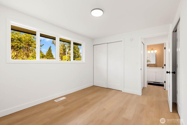 unfurnished bedroom with baseboards, light wood-style flooring, visible vents, and a closet