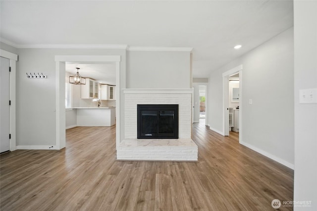 unfurnished living room with crown molding, baseboards, a brick fireplace, wood finished floors, and a notable chandelier